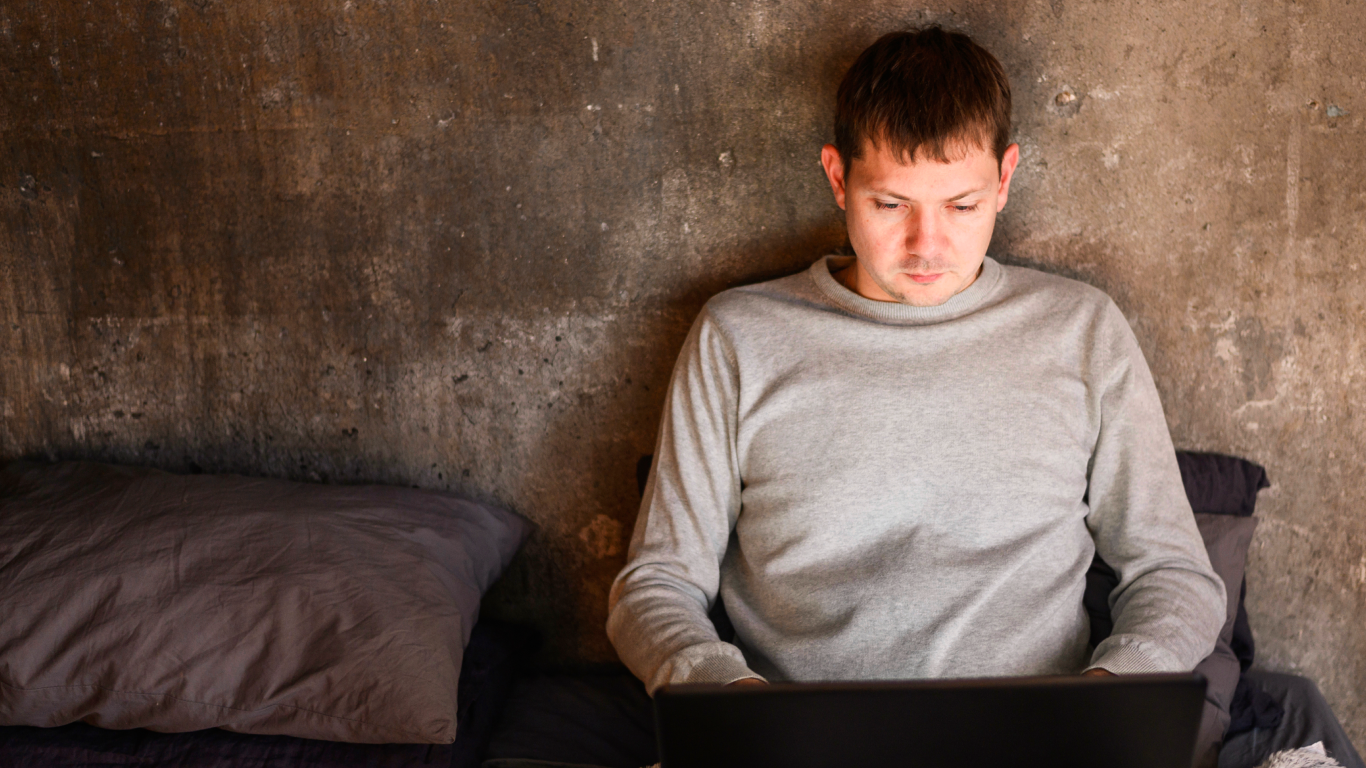 Homem na cama acessando a internet no notebook, precisando vencer o vício em pornografia
