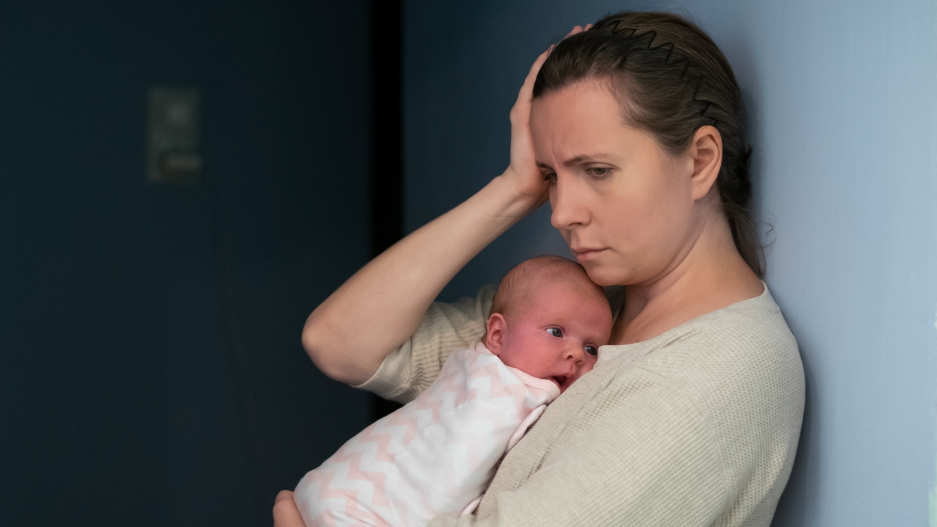 Mulher ansiosa com o bebê no colo, pensando em quanto tempo dura a ansiedade pós-parto